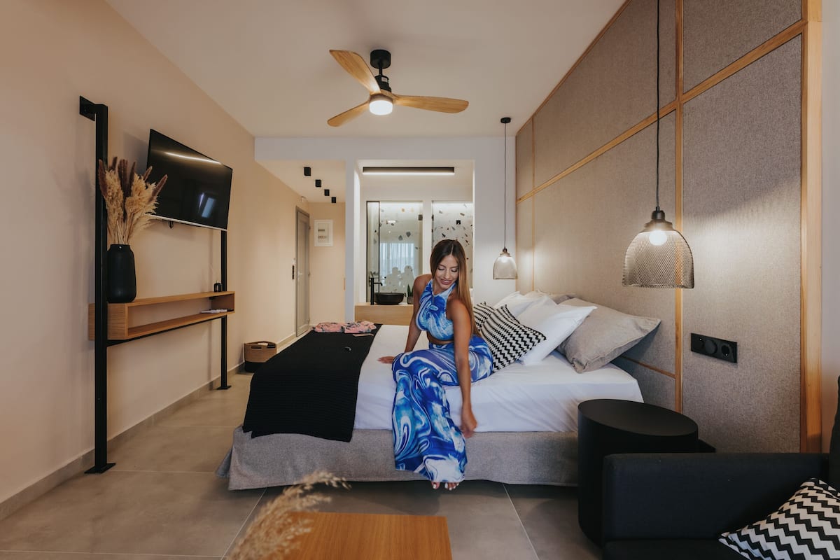 Quarto moderno com cama, televisão, ventoinha no teto e mesa de cabeceira.