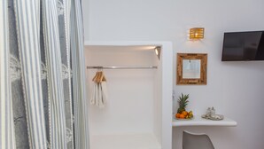 Une salle de bain moderne équipée d’une douche, d’un porte-serviettes, d’un miroir, d’un téléviseur fixé au mur et d’une petite étagère avec des fruits et un verre.