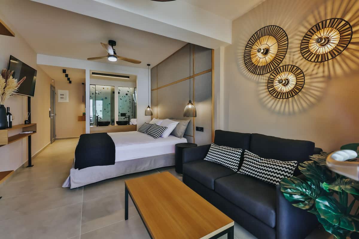 Quarto moderno com cama, mesa de cabeceira e um sofá preto com almofadas estampadas.