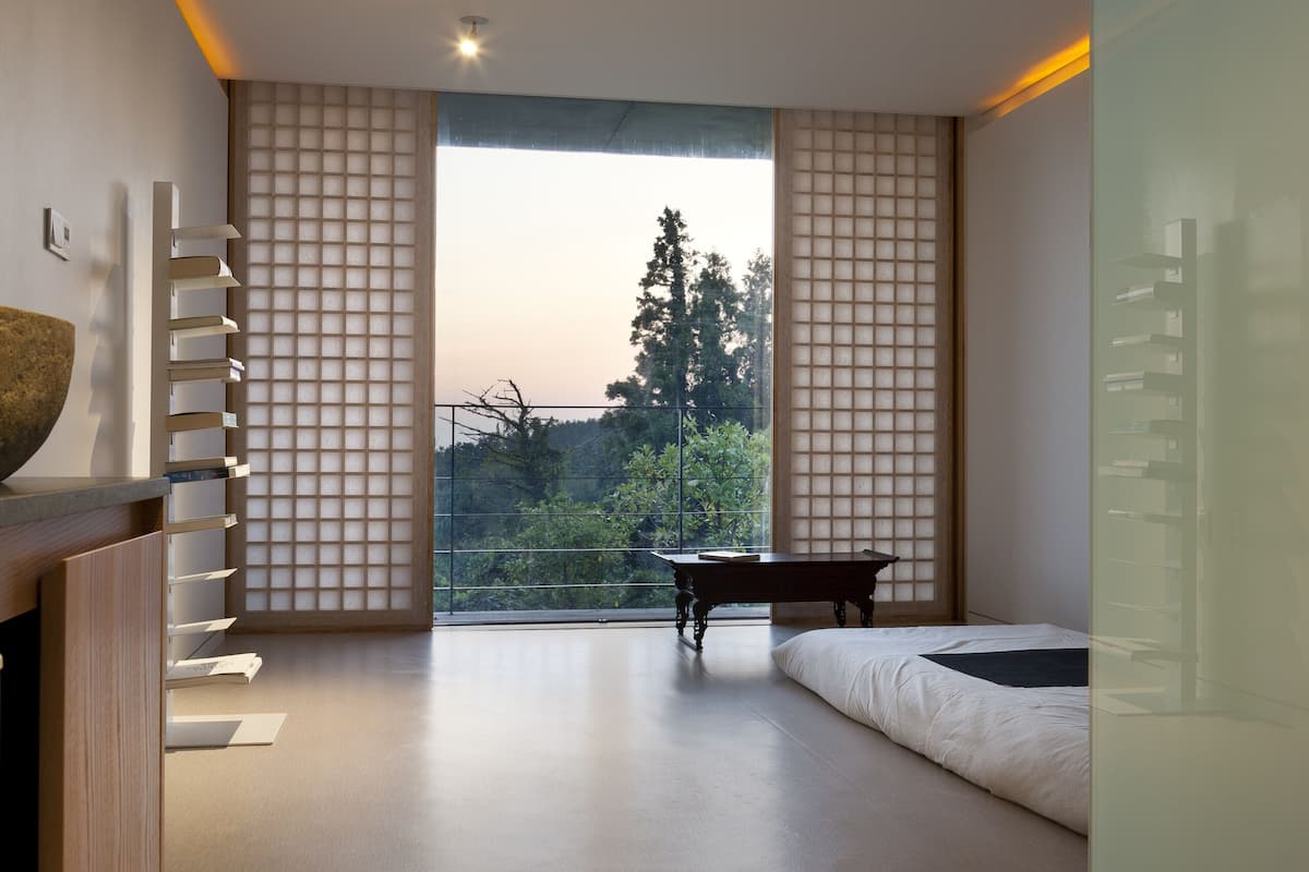 A modern room with a large window, a wooden desk, a bed, and a small table.