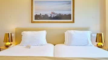 Uma cama de casal com roupa de cama branca, duas luminárias de cabeceira e um quadro na parede.