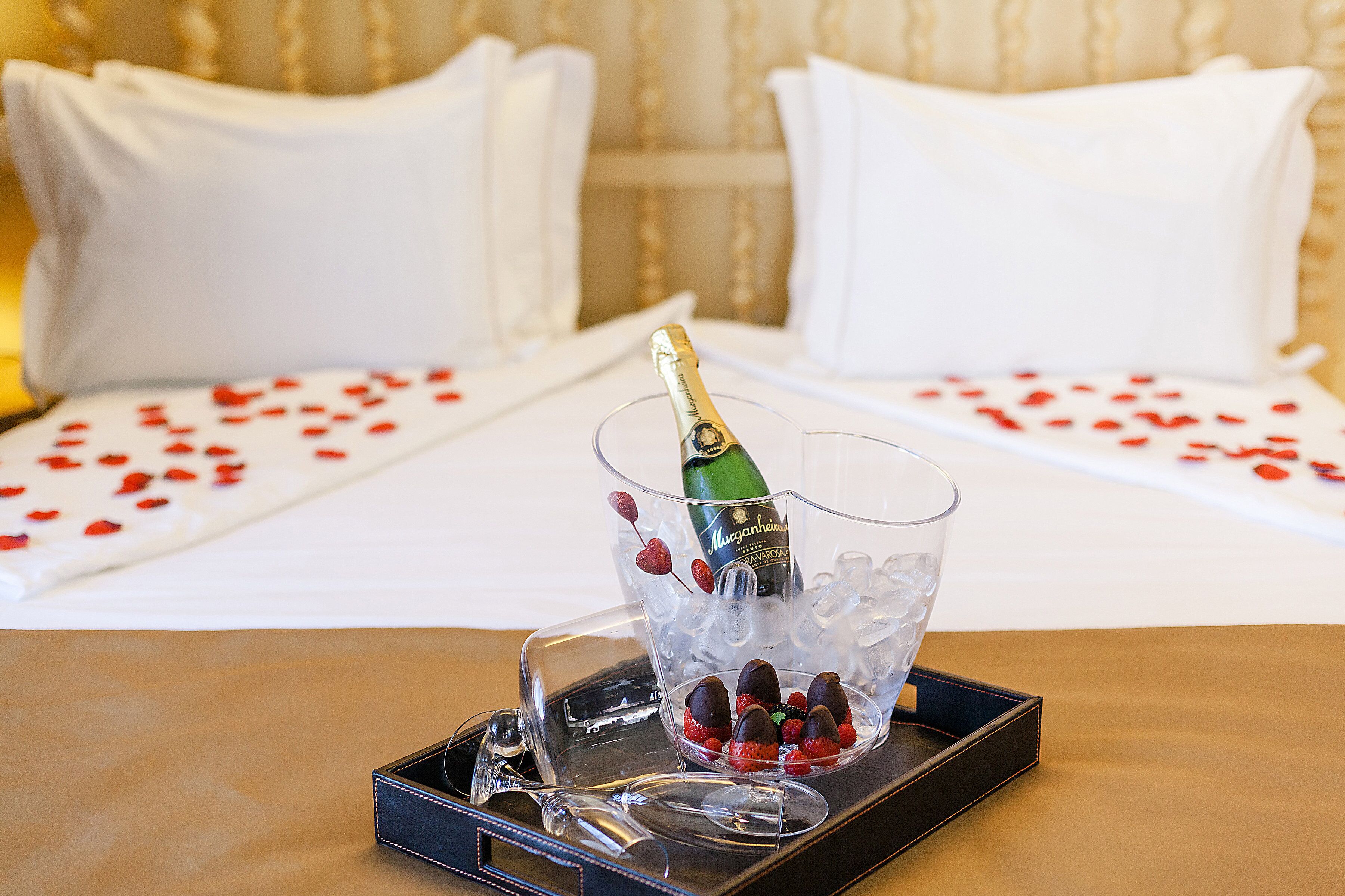 A bed with white linens and red rose petals scattered on the bedspread.