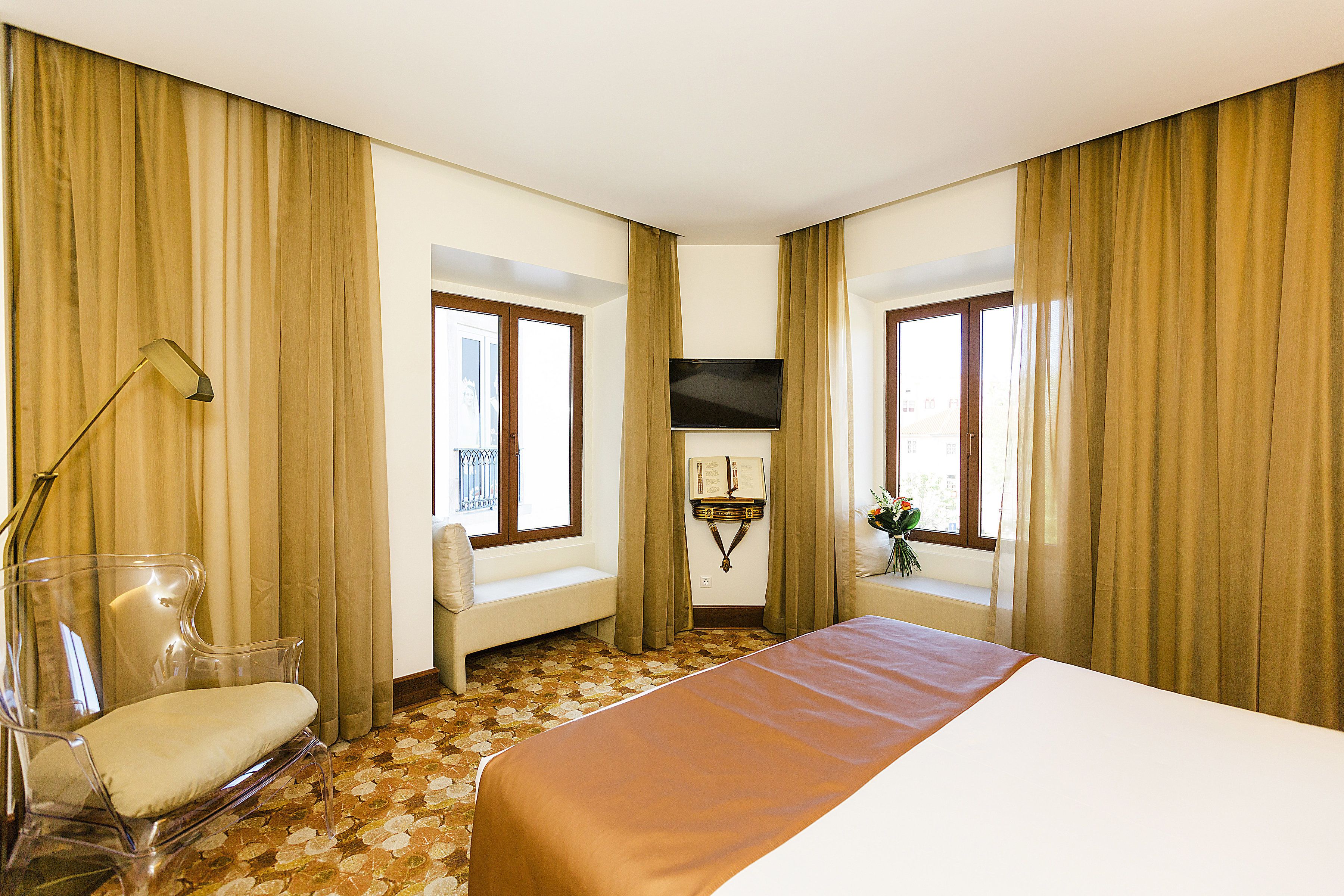 Una habitación de hotel con cama, una silla, televisión y ventana con cortinas.