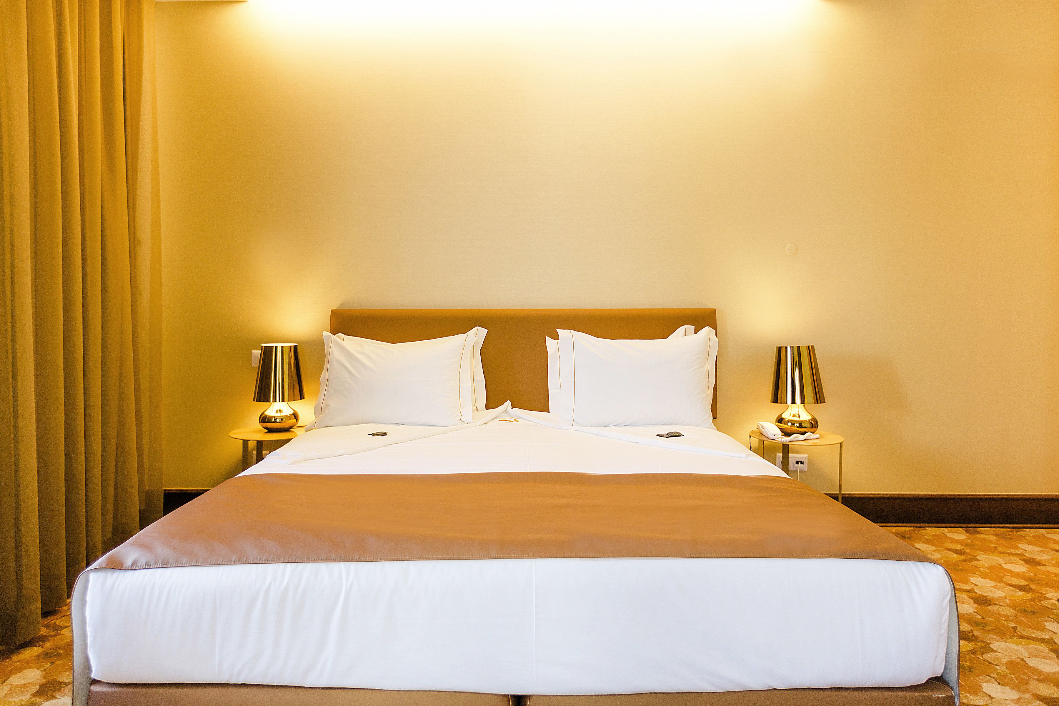 Habitación de hotel con una cama grande, dos lámparas de noche y una cortina a la izquierda.