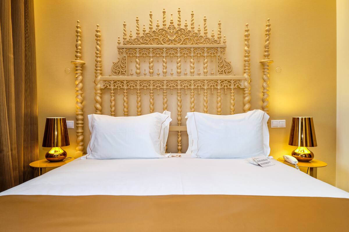 A hotel room with a large bed, two bedside lamps, a telephone, and a decorative headboard.