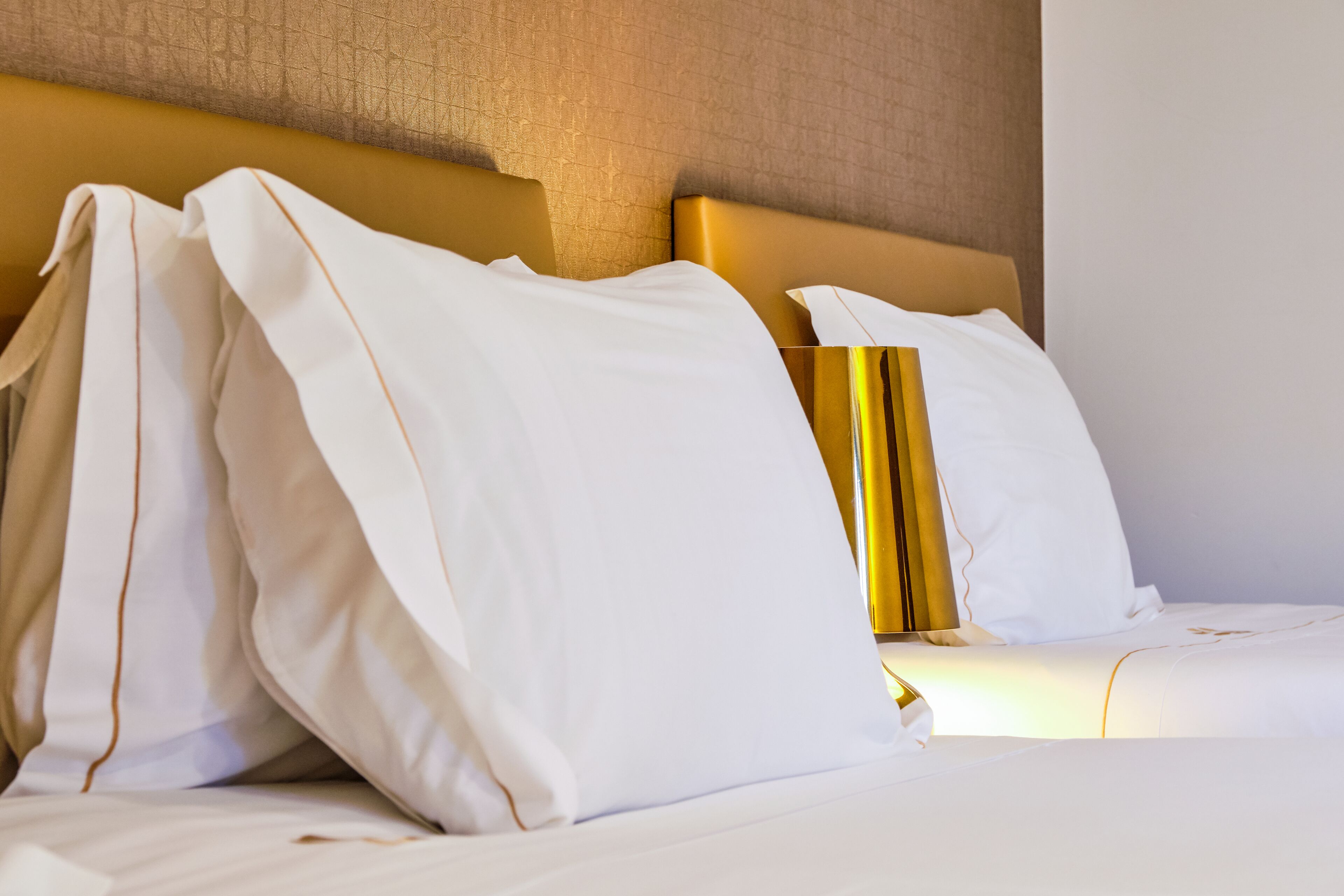 A neatly made bed with white linens and a gold headboard.