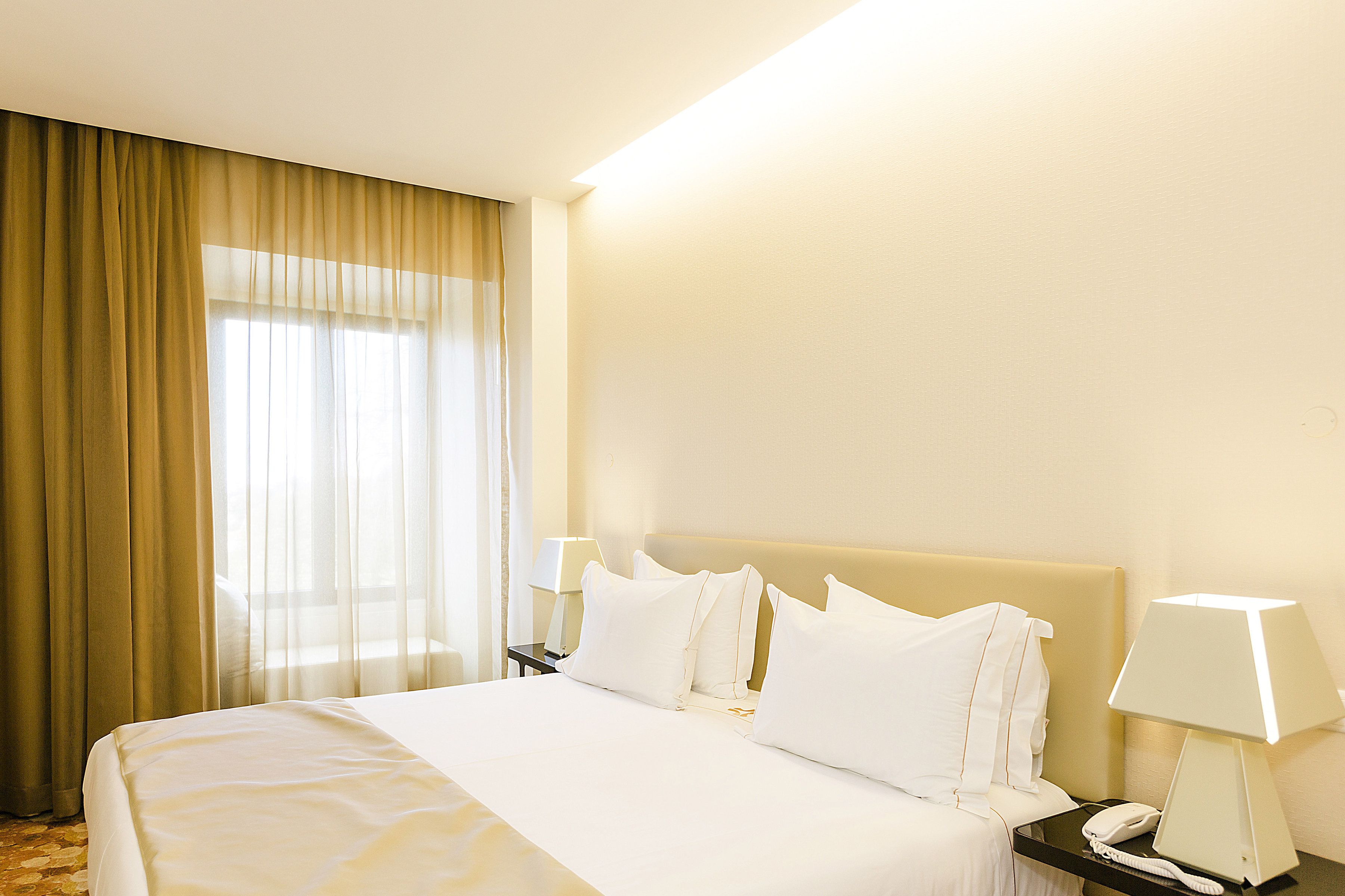 Hotelkamer met een groot bed, twee nachtkastjes met lampen en een raam met gordijnen.