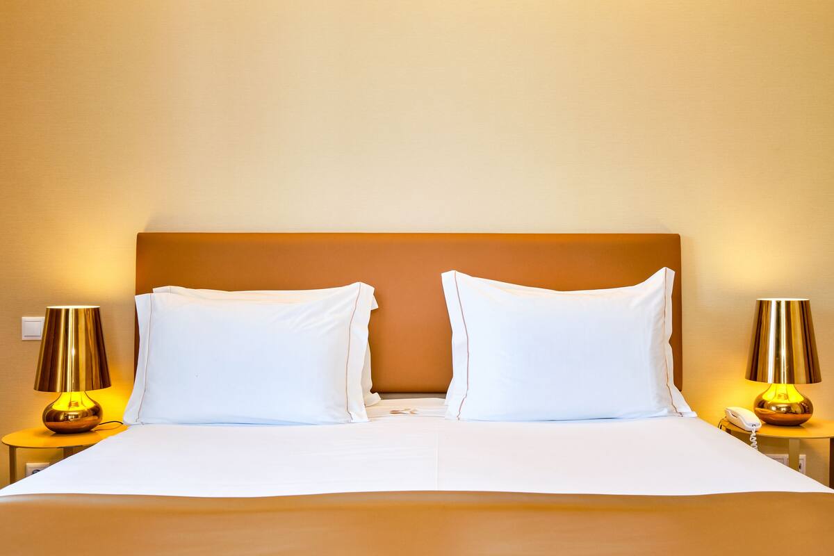 A hotel room with a large bed, two bedside lamps, and a telephone on the nightstand.