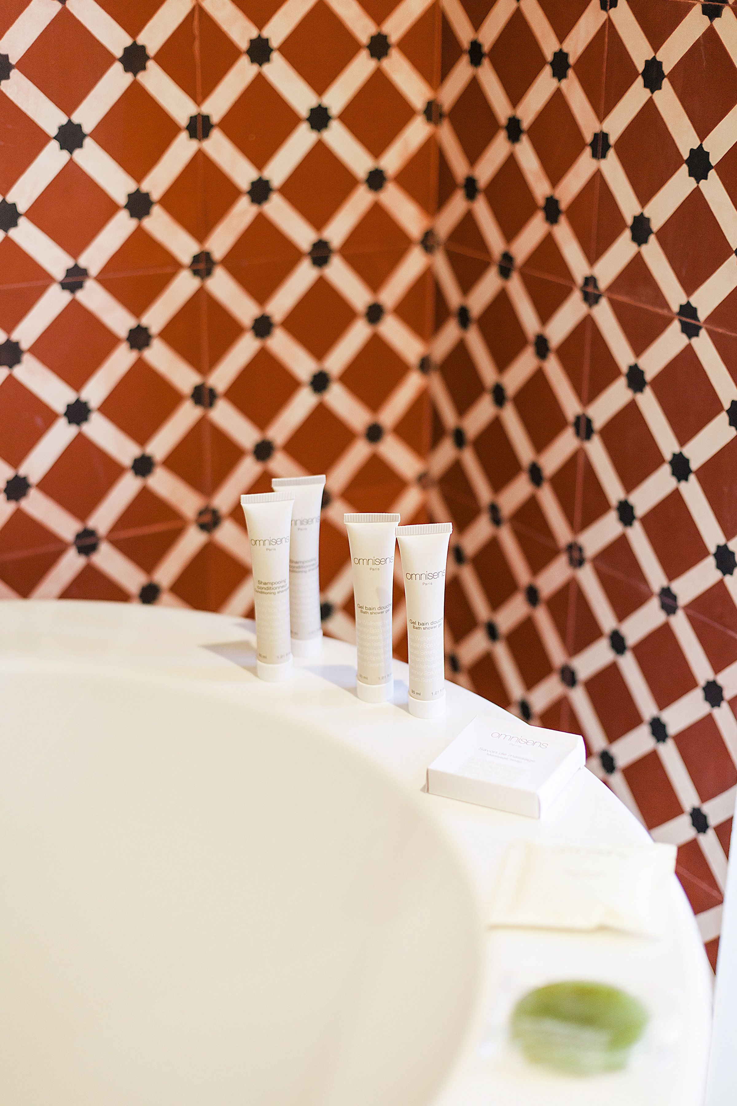 A bathroom with a patterned tile wall and three white toiletries on a white surface.