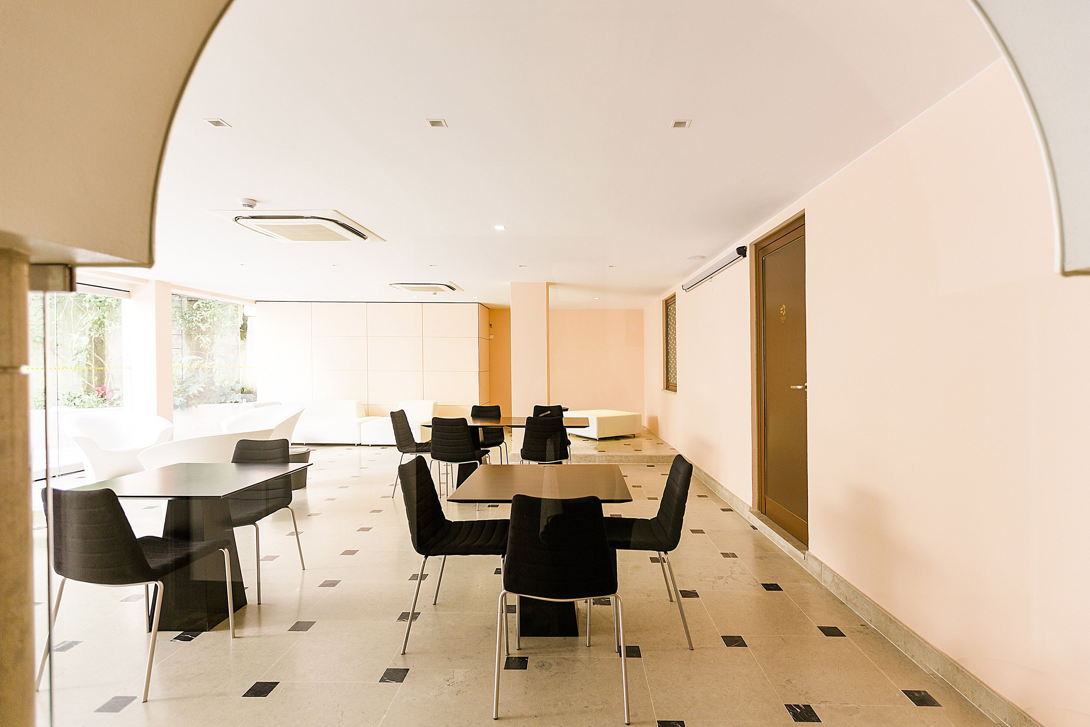 Uma sala de conferências com uma mesa de vidro, cadeiras pretas e uma porta ao fundo.
