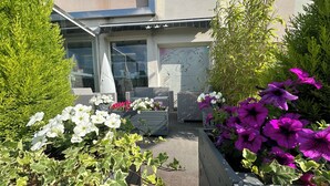 Un patio con mobiliario exterior, plantas en macetas y acceso a un edificio.