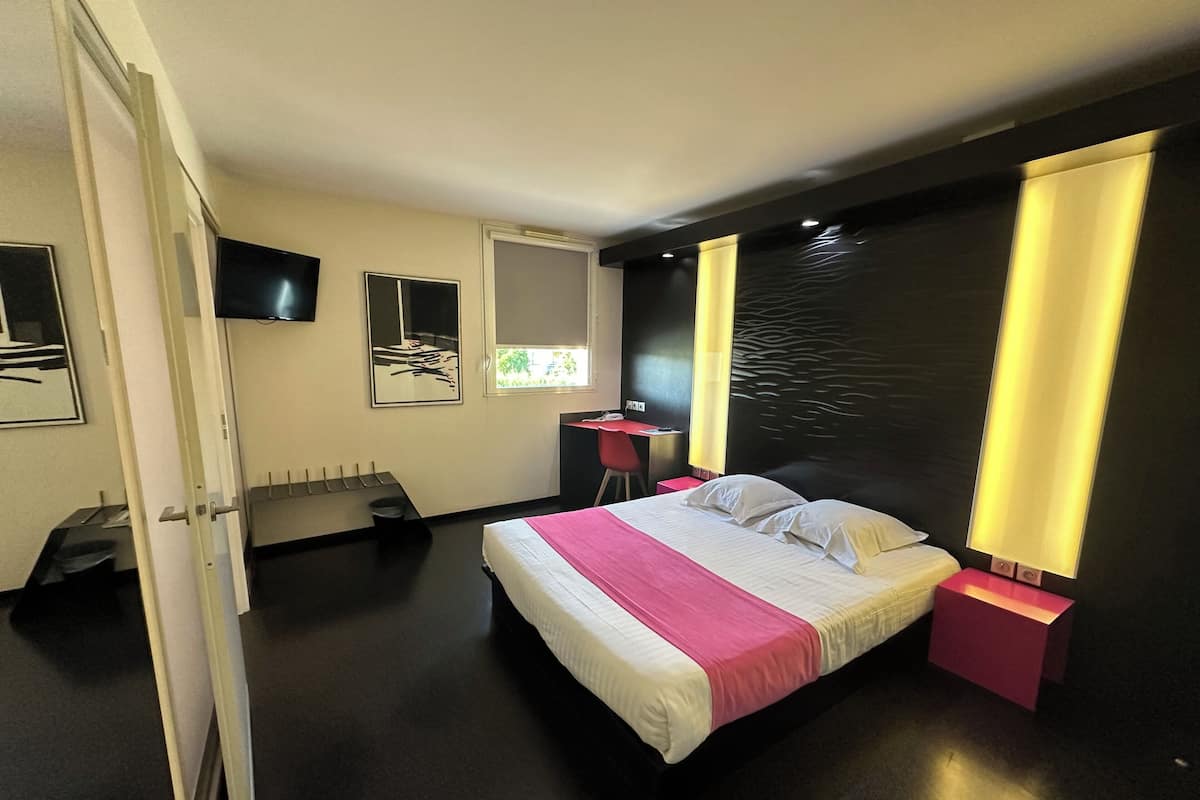 A modern hotel room with a bed, bedside tables, a desk, and a TV.