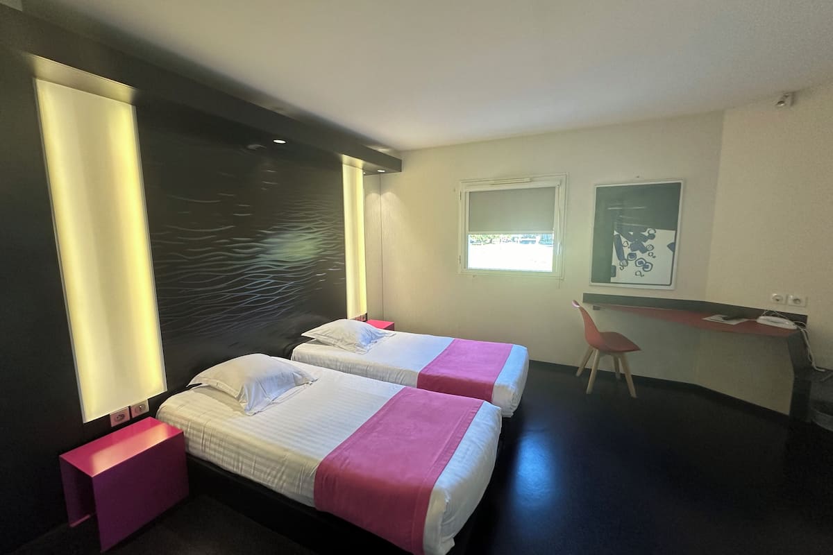 A modern hotel room with two beds, a desk, and a chair.