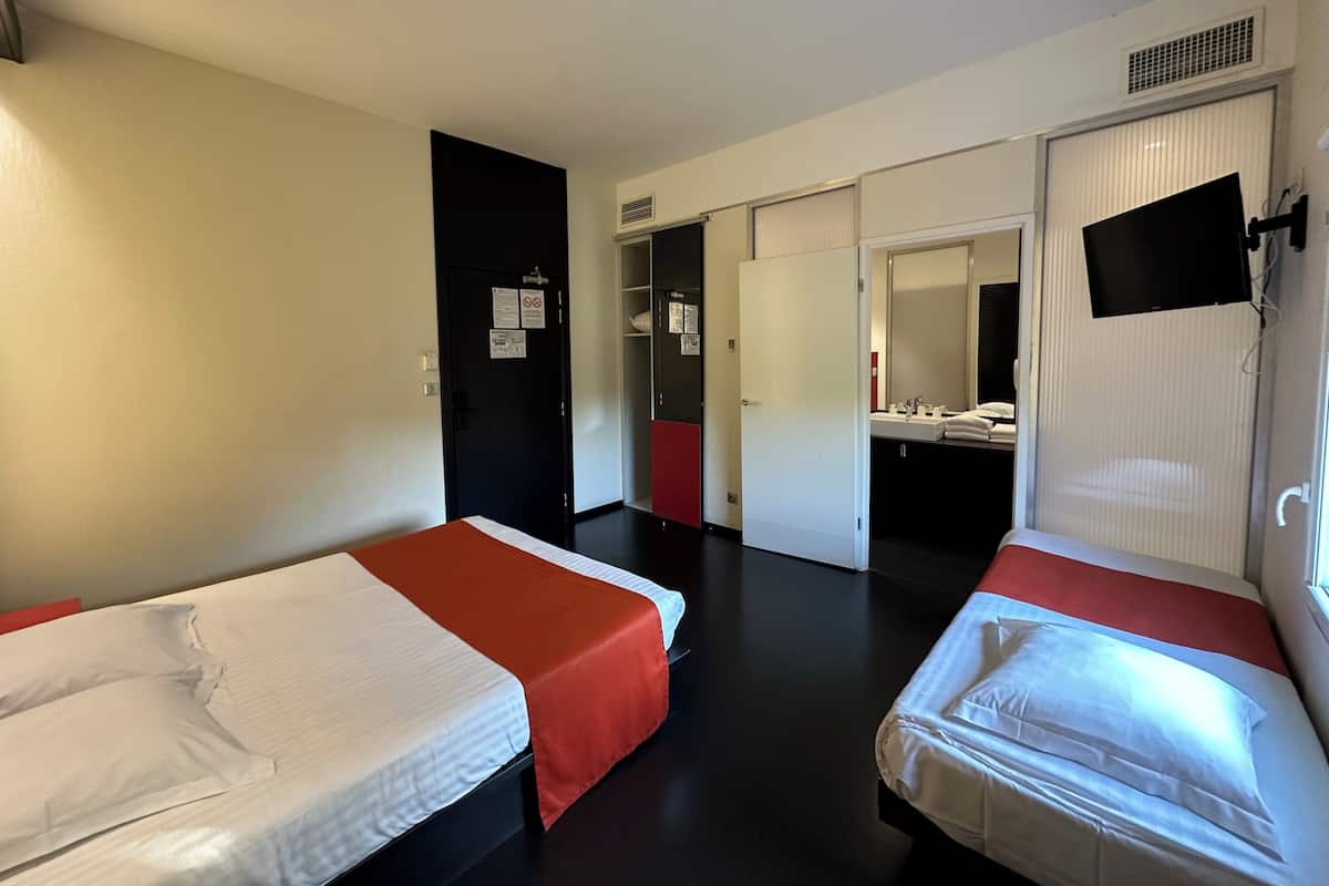 A hotel room with two single beds, a bathroom with a mirror and sink, and a wardrobe.