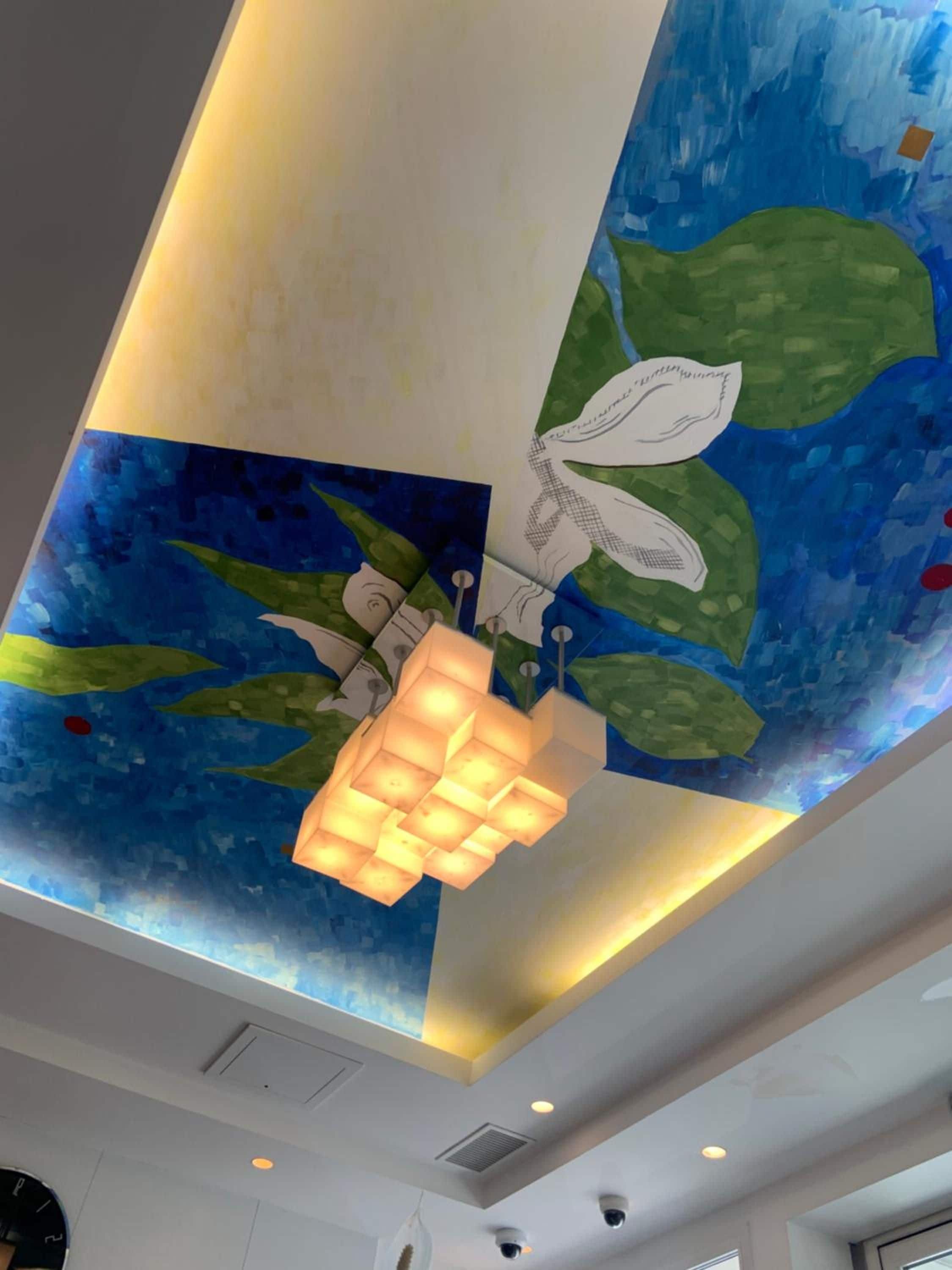 Techo con un mural pintado, iluminación empotrada y una lámpara de araña moderna.