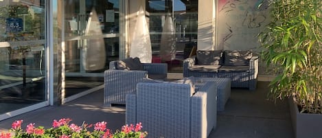 Un espace extérieur moderne, aménagé avec des meubles en osier et doté d’une entrée en verre.