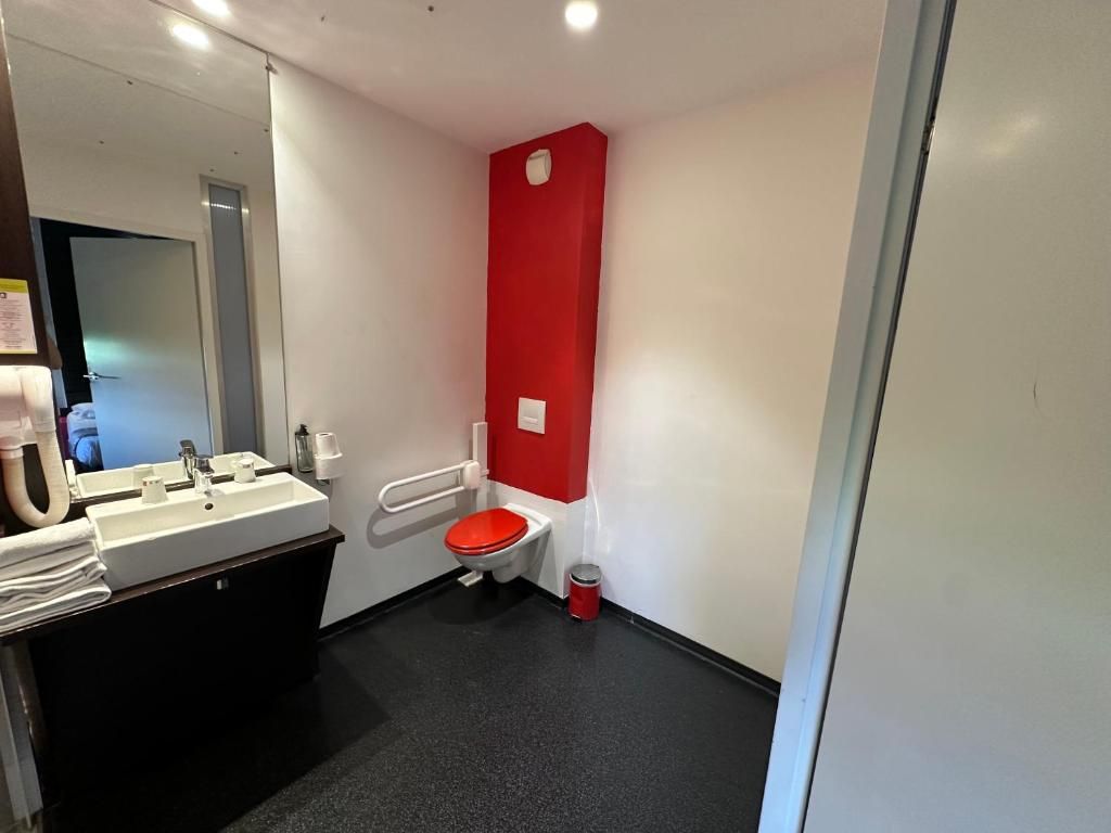 Ein Badezimmer mit einem weißen Waschbecken, einer roten Toilette und einem Spiegel.
