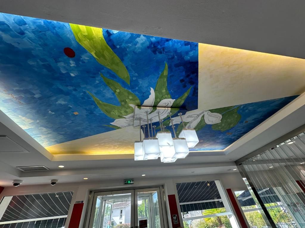 A ceiling with a painted mural, a modern chandelier, and a view through a glass door.