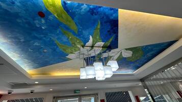 A ceiling with a painted mural, a modern chandelier, and a view through a glass door.