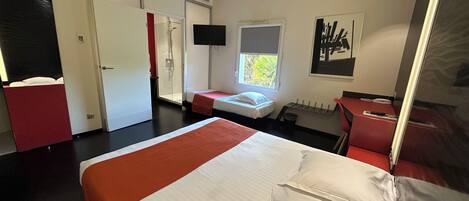 A hotel room with a large bed, a shower area, a small desk, and a window with a view of greenery.
