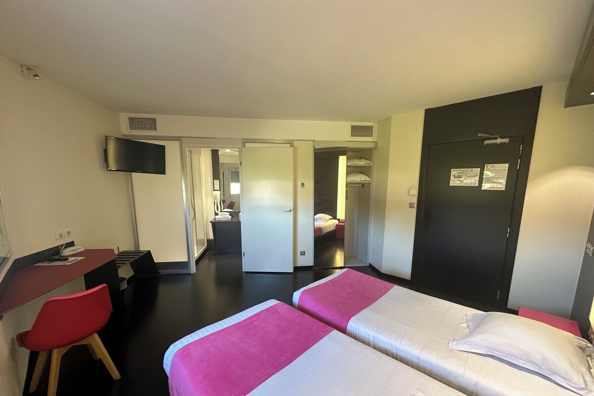Habitación de hotel con dos camas, un escritorio, una silla, un televisor y un armario.