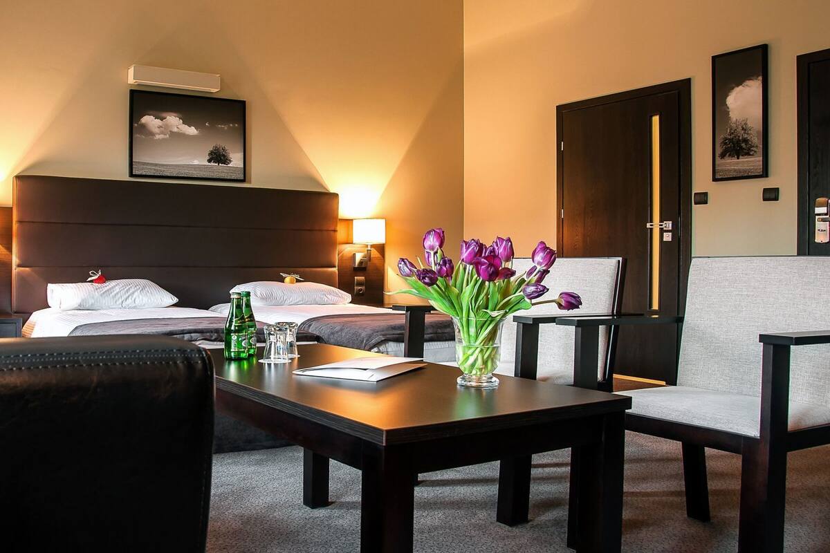 A hotel room with a bed, two bedside tables, a desk with a vase of flowers, a chair, and a sofa.