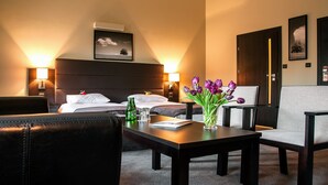 Ein Hotelzimmer mit einem Bett, zwei Nachttischen, einem Schreibtisch mit Blumenvase, einem Sessel und einem Sofa.