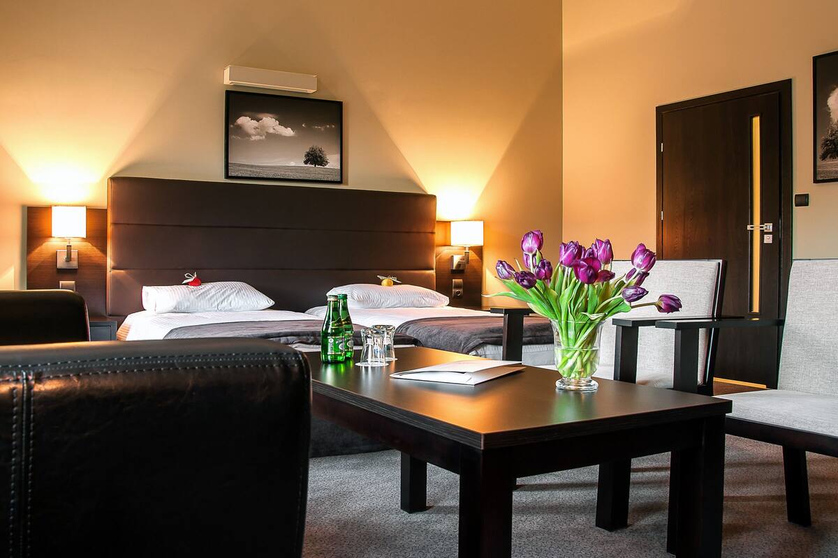 A hotel room with a bed, two bedside tables, a desk with a vase of flowers, a chair, and a sofa.