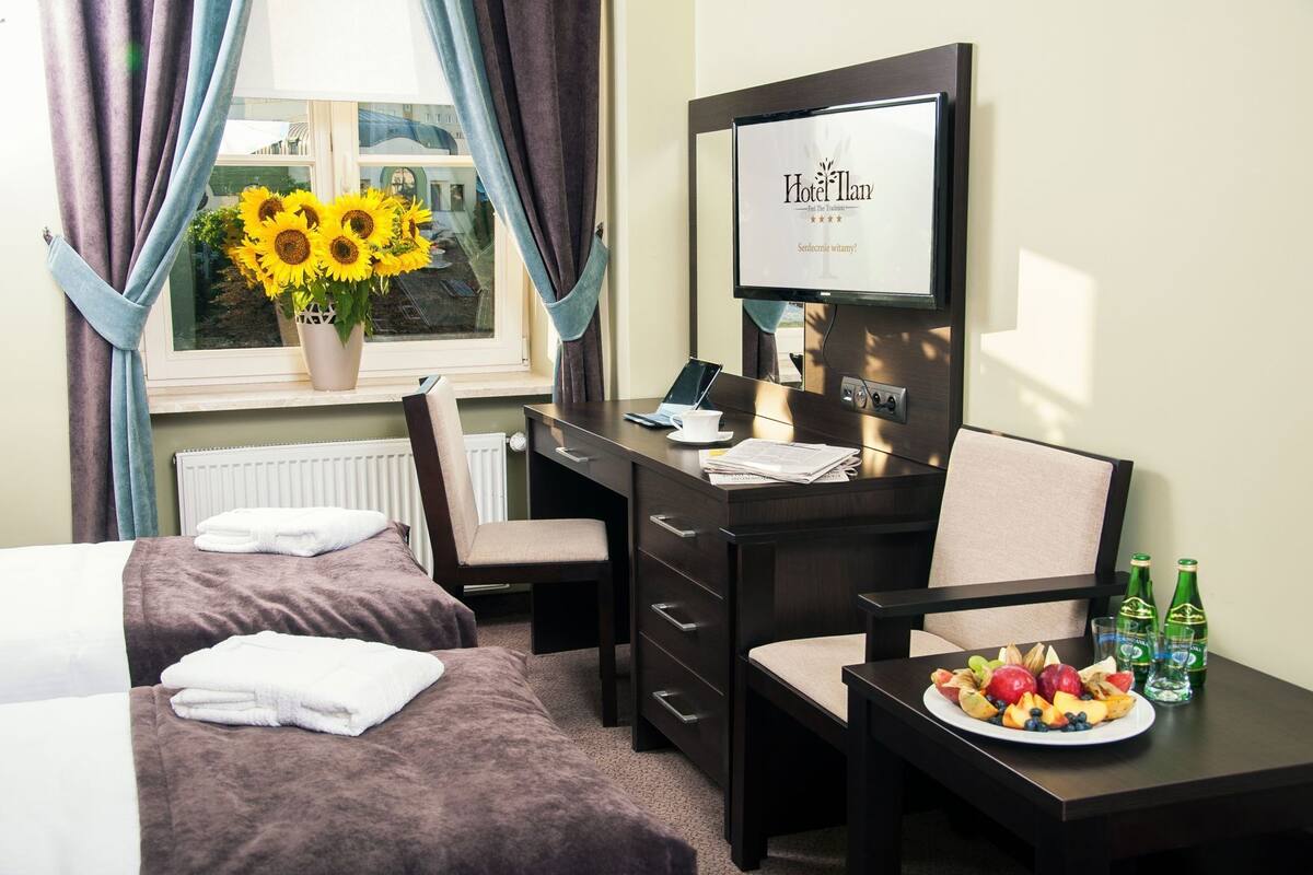 A hotel room with two beds, a desk with a laptop, a TV, and a fruit plate.