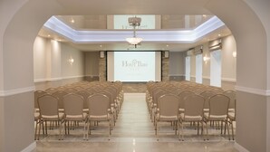 Ein Konferenzraum mit Reihen von Stühlen, einer Projektionsleinwand mit 'Hotel Ilan' und einer Kristallleuchter.