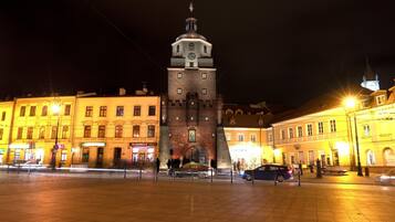 A historic tower with a clock, surrounded by well-lit buildings and a paved square.