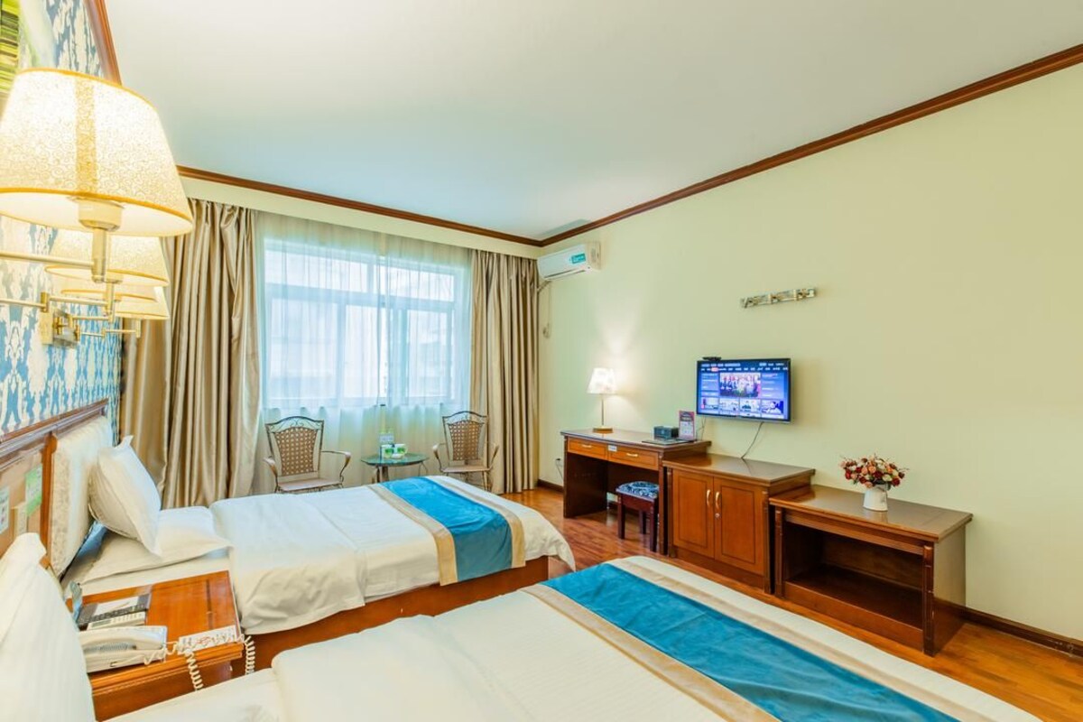 A hotel room with two beds, a desk, a television, and a window with curtains.