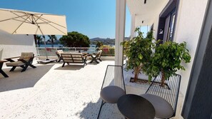 Une terrasse avec des sièges extérieurs, une vue sur la mer et un bâtiment doté d’un balcon.