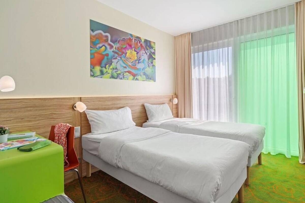 A hotel room with two beds, a painting on the wall, a desk with a lamp, and a TV on the wall.