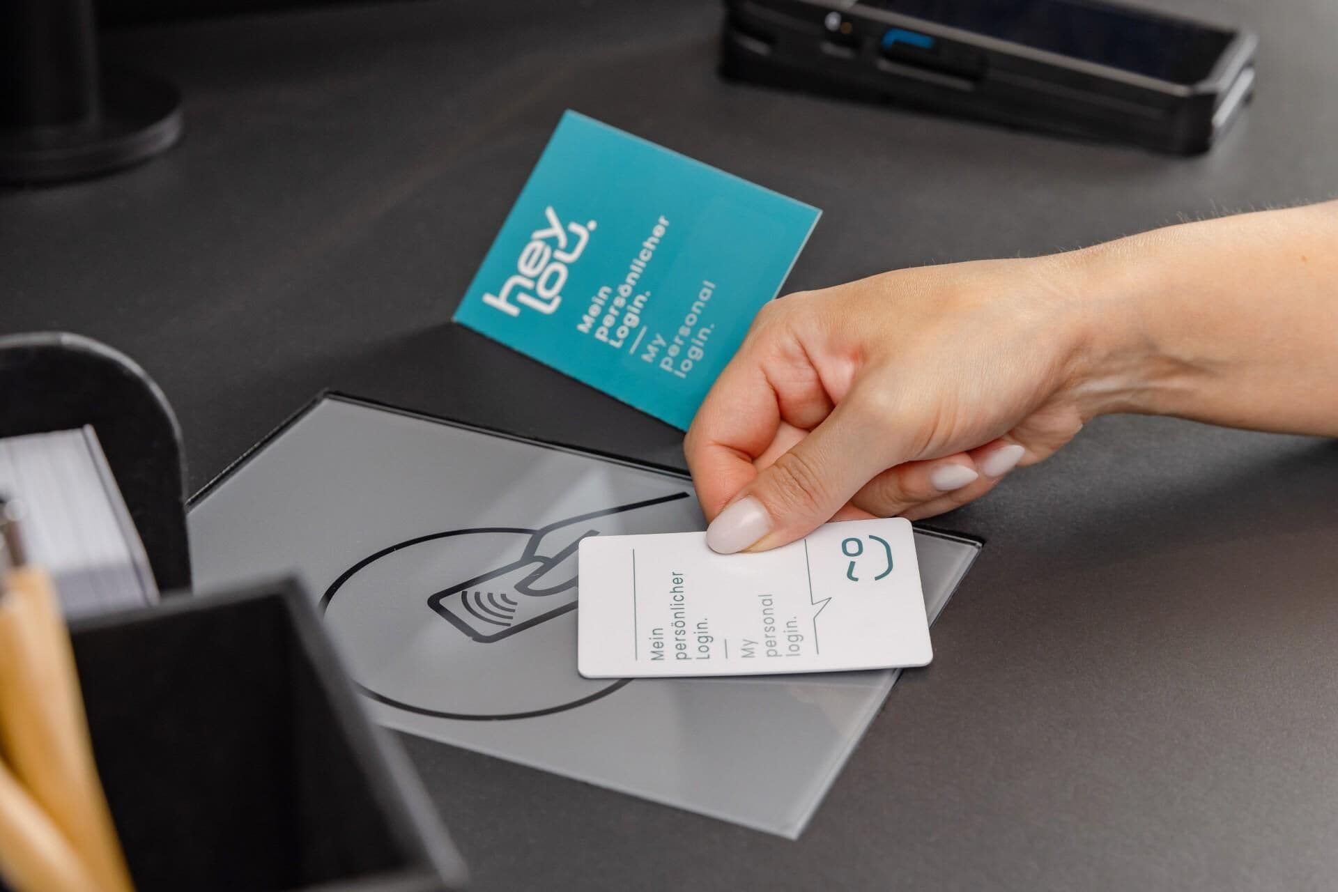 A hand holding a card with a logo and text, placed on a table with a blue card and a grey envelope.