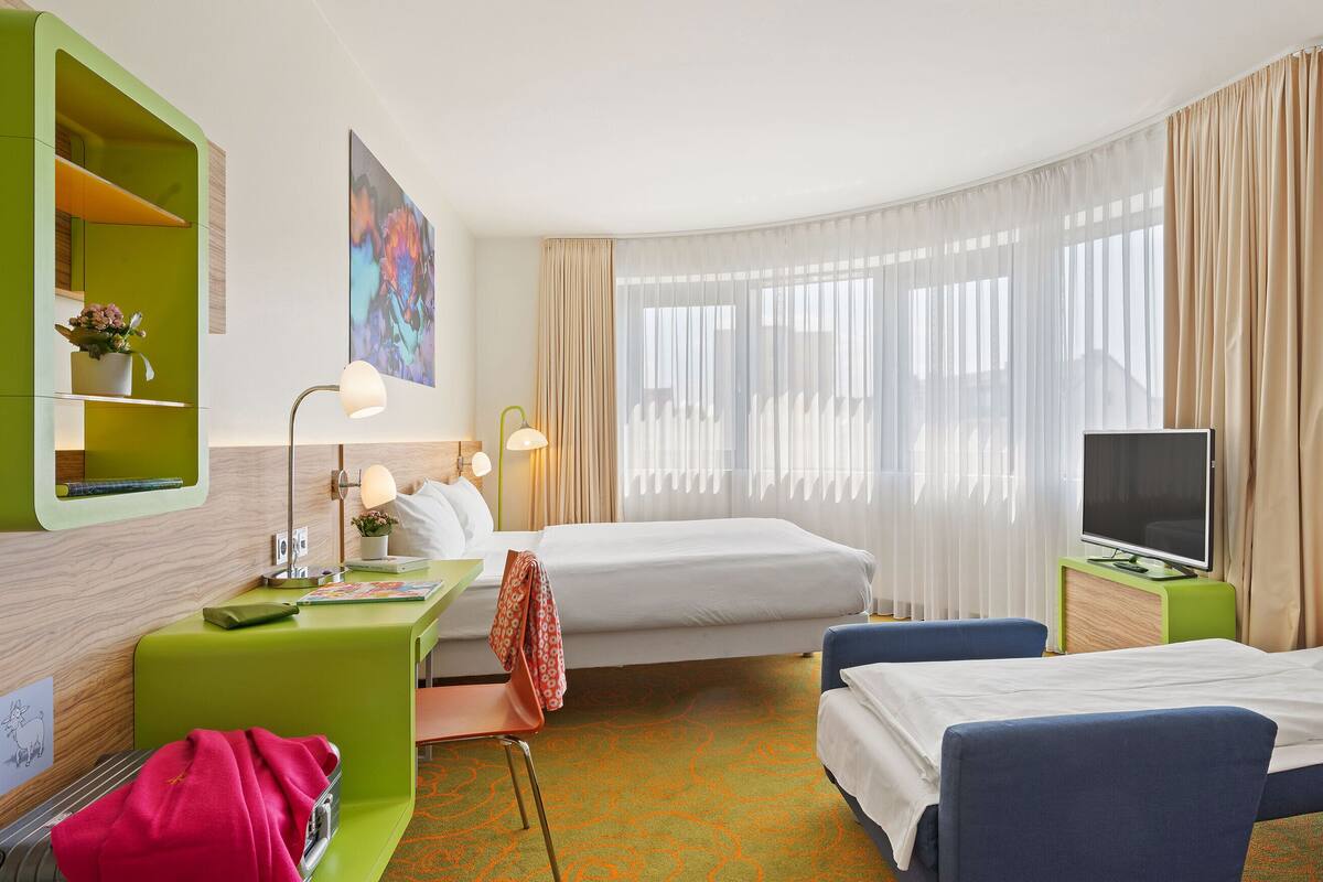 A hotel room with a bed, a desk with a computer, a TV, and a chair.
