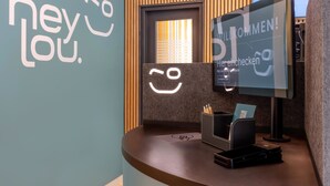 Uma receção com um monitor a exibir 'WILLKOMMEN!' e uma parede com o texto 'hey Lou'.