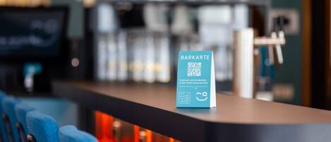 Zona de bar con un cartel de código QR, taburetes y una barra.