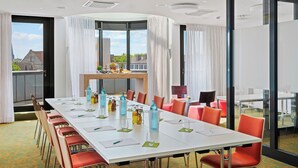 Une salle de conférence avec une longue table, des chaises et une petite table sur laquelle se trouvent un panier de fruits et des bouteilles.