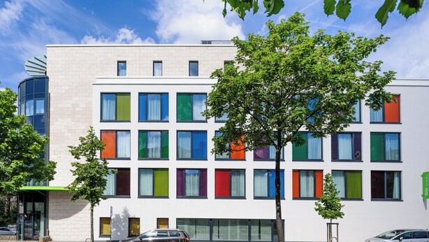 Un bâtiment moderne à la façade blanche, doté de nombreuses fenêtres et surmonté d’un auvent vert.
