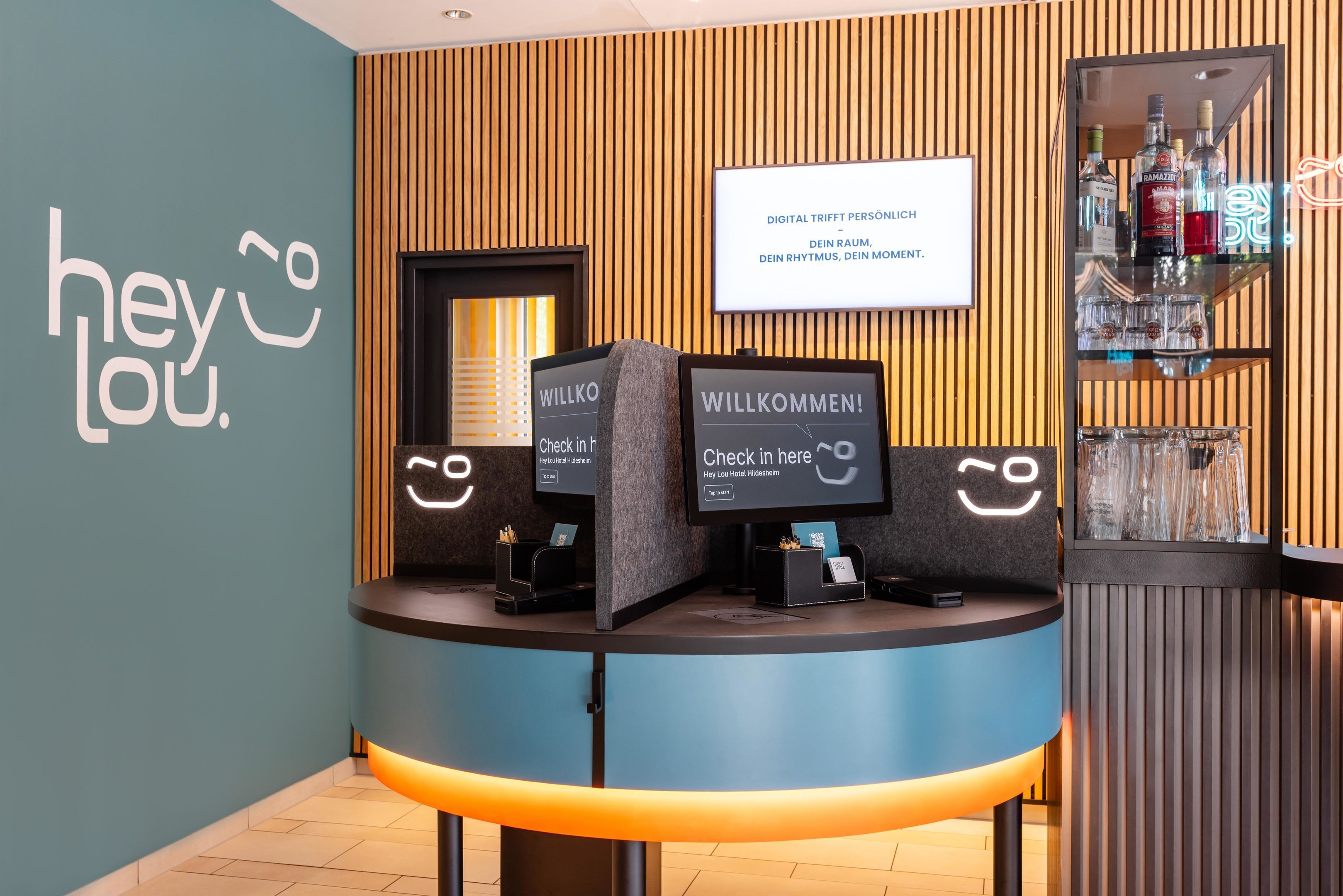 A reception desk with a sign that reads 'WILLKOMMEN!' and a digital screen displaying 'Check in here'.