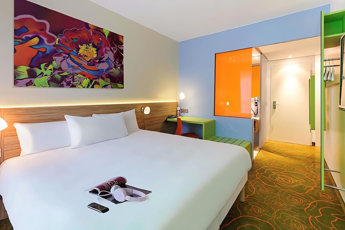 Habitación de hotel con una cama grande, un cuadro en la pared, un baño con espejo y una pared de acento verde.