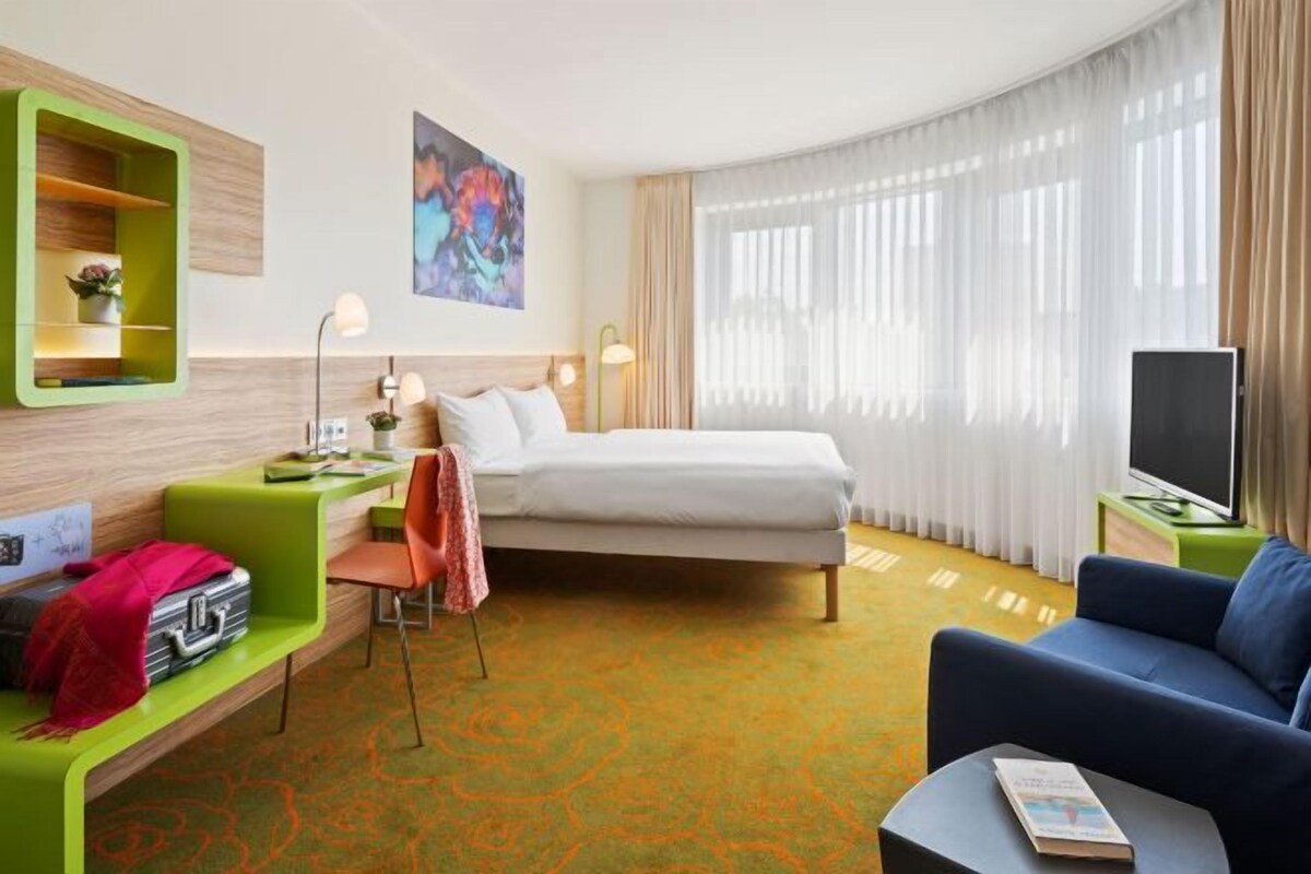 Una habitación de hotel con cama, escritorio con silla, televisor y sofá.