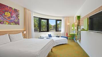 Ein Hotelzimmer mit zwei Betten, einem großen Fenster, einem Bild und einem grünen Schreibtisch.