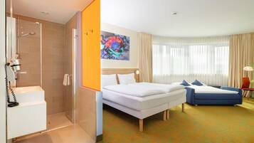 A hotel room with a shower, a bed, a bedside table, a lamp, and a window with curtains.