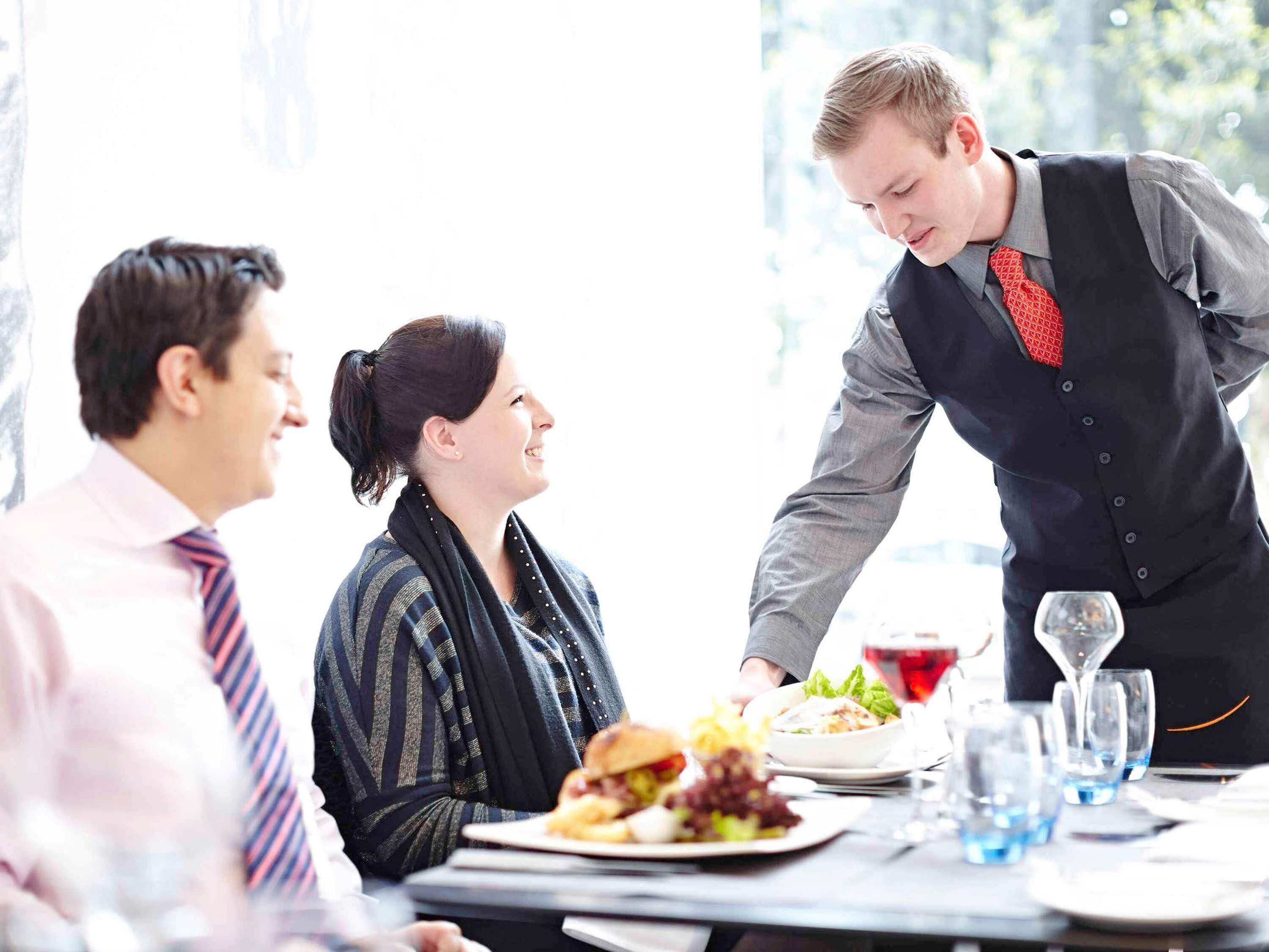 A dining table with plates of food, glasses, and a waiter serving.