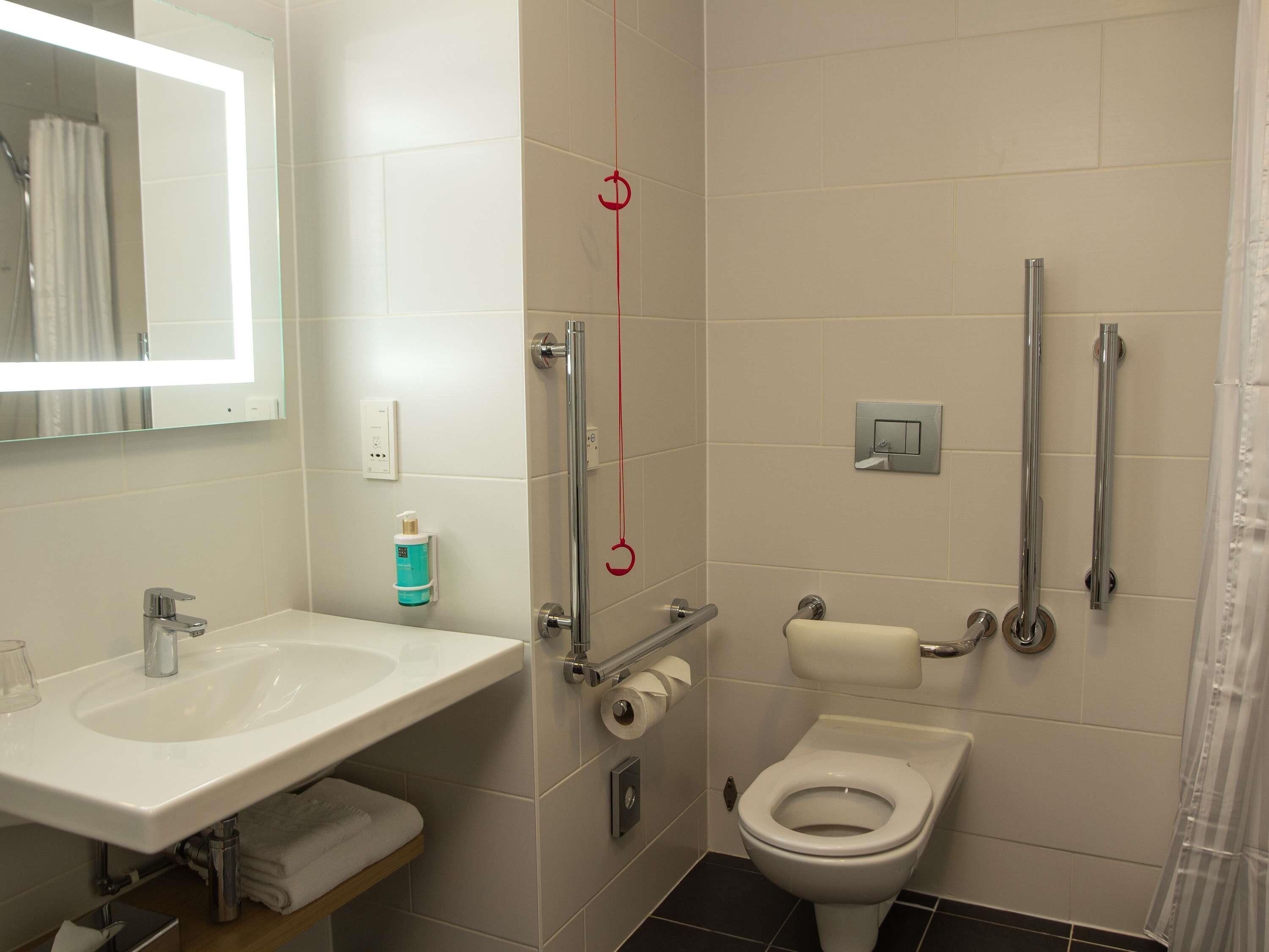 Ein Badezimmer mit Waschbecken, Spiegel, Toilette und Haltegriffen.