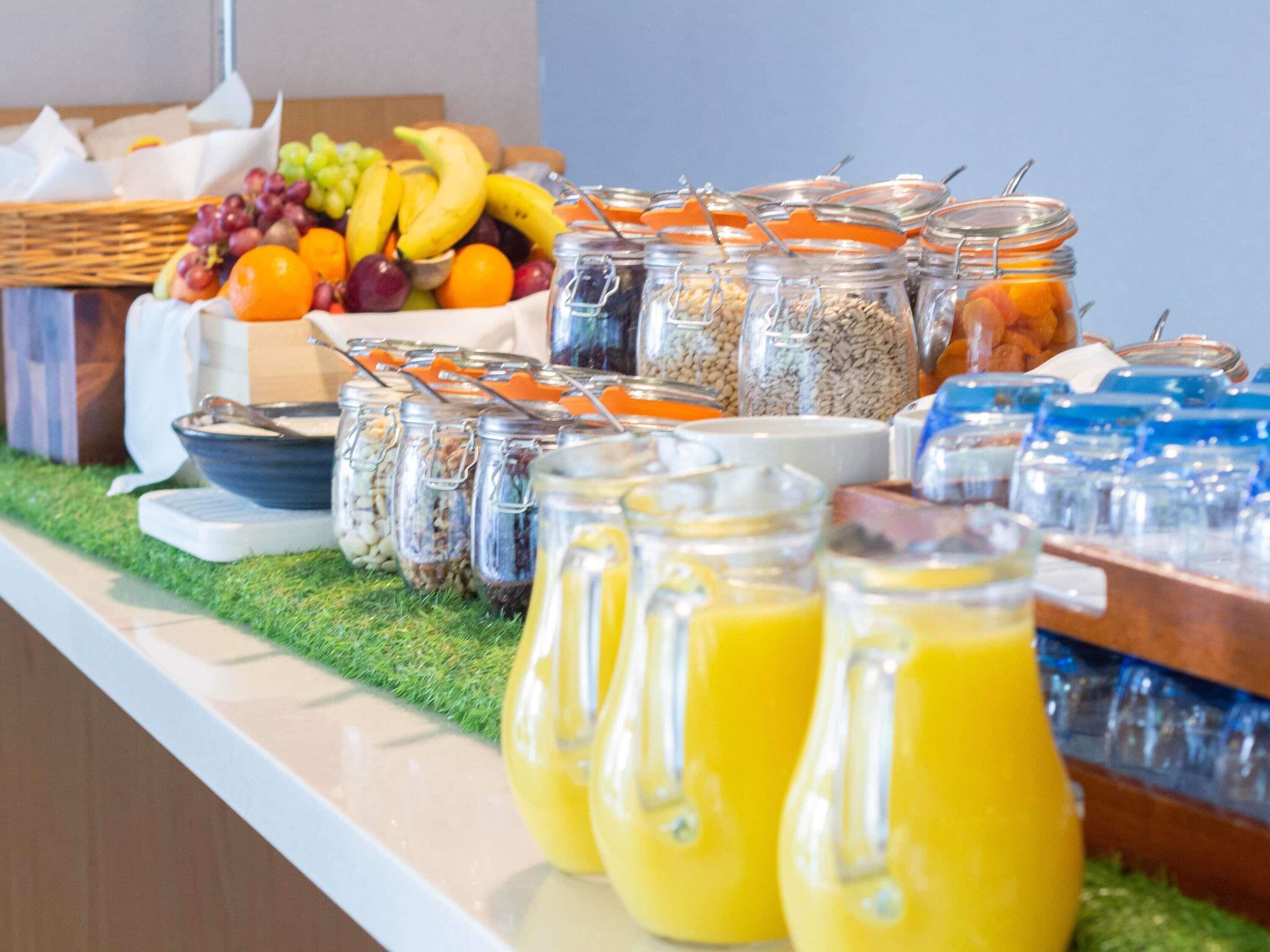 Un buffet proposant une variété d’aliments, notamment des fruits, des céréales et du jus d’orange.