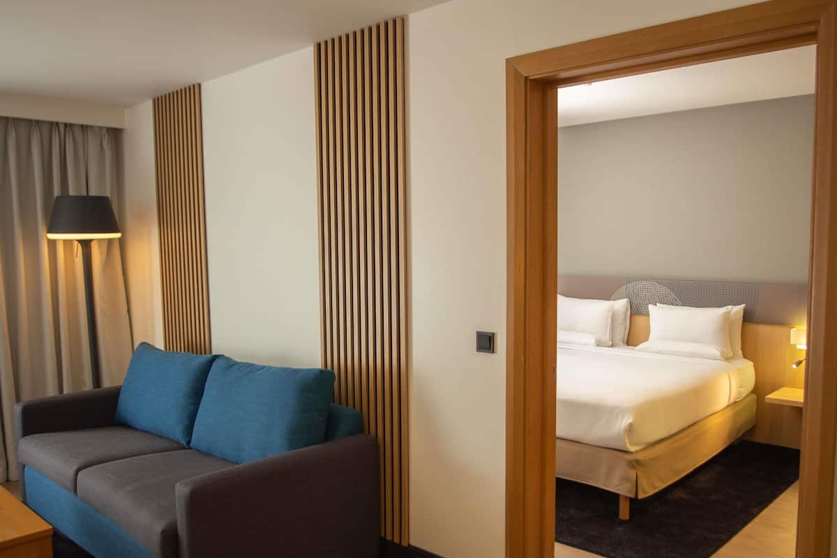 Hotellihuone, jossa on sohva, sänky, lamppu ja puupanelilla verhoiltu seinä.