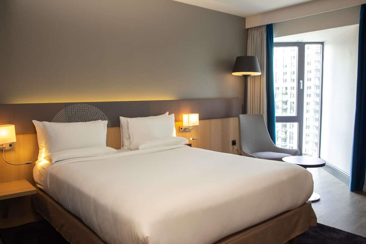 Hotellihuone, jossa on suuri sänky, tuoli, pieni pöytä ja ikkuna, jossa on verhot.